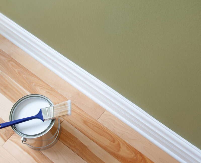 Paintbrush and an open can of white paint on wooden floor Painting Services
